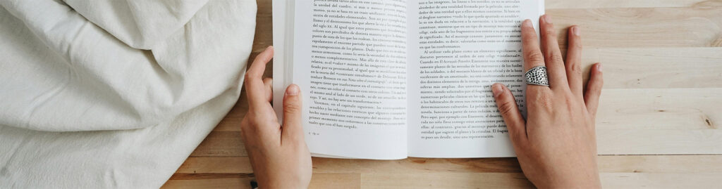 Image of two hands holding a book flat on a pine wood table reading a self help book