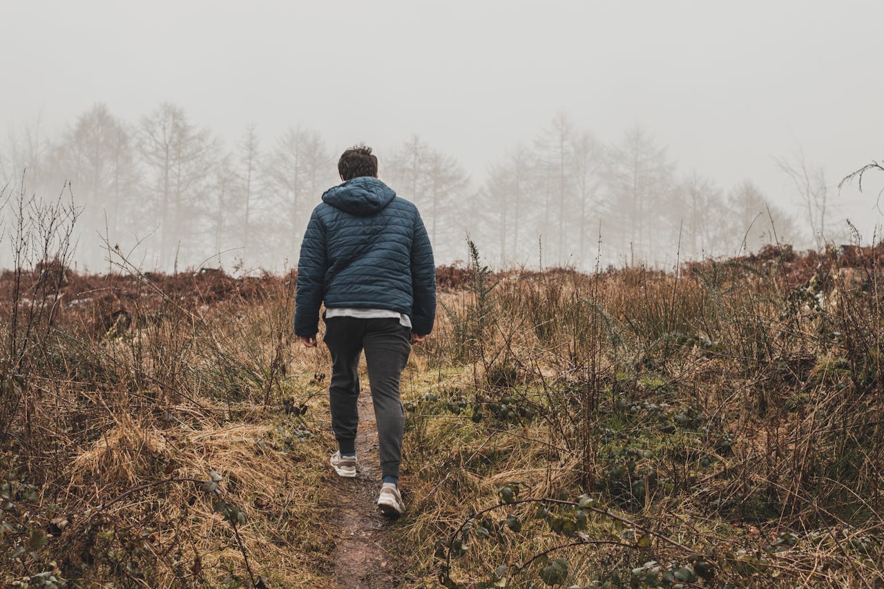 A person walking up a grass embankment towards a forest looking content and happy.